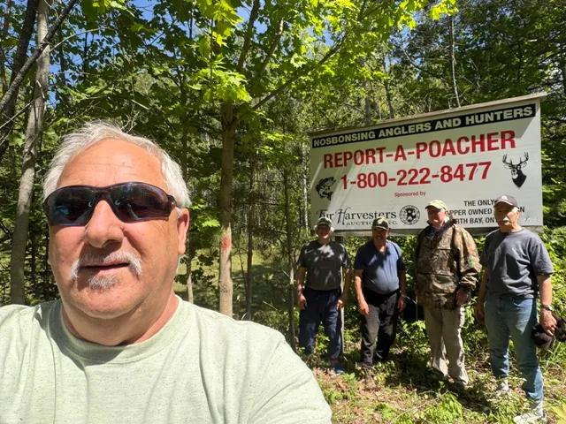Rick Champagne with Nosbonsing Anglers and Hunters beside a Report a Poacher sign